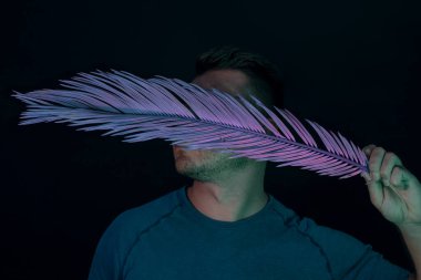 Genç adam yüzünü neon ışıkla kaplamış. Siyah üzerine. Minimalizm retro tarzı konsept.