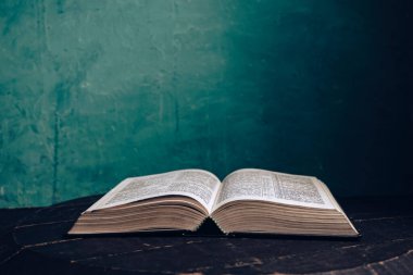 Kahverengi meşe ağacından yapılmış eski bir masanın üzerinde güzel, açık kutsal bir İncil. Yeşil duvar arkaplanı.