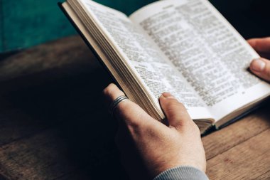 İncil 'i okuyan bir adam eski bir meşe ağacından masa ve yeşil duvar arka planında..