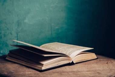 Açık antika bir kitap. Tasarım için model arka planı. Yuvarlak meşe ağacından bir masa ve yeşil duvar arkaplanı..