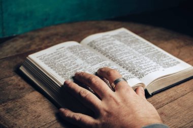 İncil 'i okuyan bir adam eski bir meşe ağacından masa ve yeşil duvar arka planında..