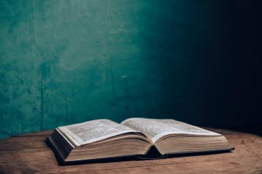 Kahverengi meşe ağacından yapılmış eski bir masanın üzerinde güzel, açık kutsal bir İncil. Yeşil duvar arkaplanı.