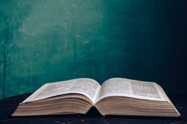 Kahverengi meşe ağacından yapılmış eski bir masanın üzerinde güzel, açık kutsal bir İncil. Yeşil duvar arkaplanı.