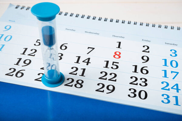 Маленькие песочные часы стоят на календаре, считая время. Концепция крайнего срока реализации проектов, подход к назначению, скоротечность времени