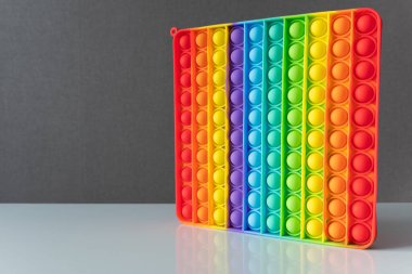 Kare modayı takip eden çok renkli çocuklar parmak bastırma baloncukları için Popit antistresi kullanıyor. Motor becerilerin gelişimi, eğlence eğlencesi. Yan görünüm, beyaz yüzeyde duruyor, gri arkaplan.