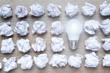 Buruşuk ofis kağıdı ve ahşap masa üzerindeki ampulle yeni bir konsept fikri. Doğru çözümü bulmak, beyin fırtınası