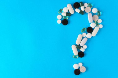 Bazı haplar mavi arka planda soru işareti şeklinde yatar. İlaç, tedavi, teşhis seçimi konsepti