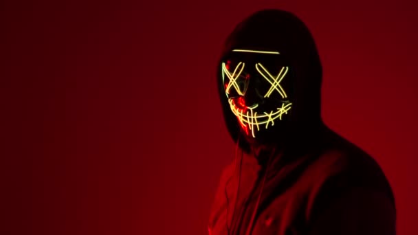 Anonym schüttelt den Kopf, Halloween-Maske, unbekannte Horrorfilmfigur, maskierter Bösewicht. Ein Mann in einer Maske in Neonlicht auf rotem Hintergrund. Ein Mann in einer Maske im Neonlicht auf rotem Hintergrund — Stockvideo