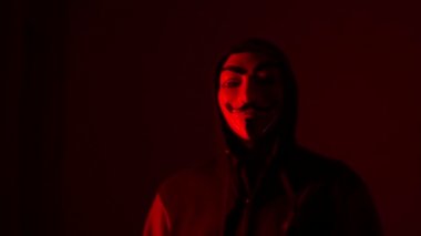 Maskeli ve kapüşonlu kimliği belirsiz bir adam tehditkar bir el hareketi yapıyor. Cadılar Bayramı partisi, kırmızı ışıkta maskeli kötü adam. Korku filmi kahramanı.