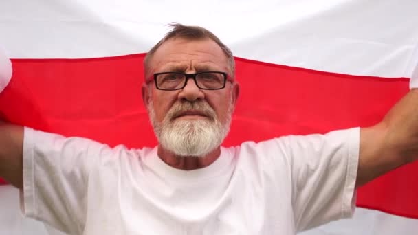 Zbliżenie portret siwy emeryt z okulary i broda, trzymam czerwienno-biały sztandar Białoruś. Protesty na Białorusi, rewolucja kolorów — Wideo stockowe