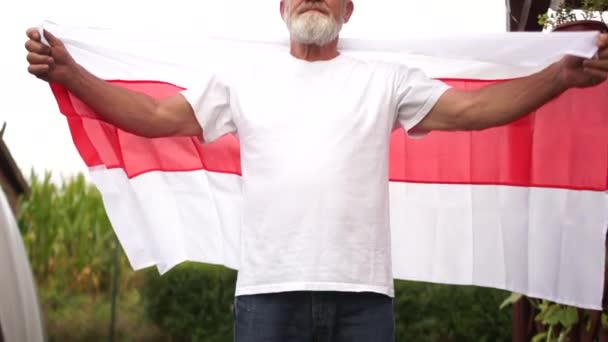 Διαδήλωση στη Λευκορωσία. Ένας άνδρας κρατά τη σημαία της Λευκορωσίας και την απλώνει με τα χέρια του σε μήκος στο φόντο του ουρανού και του ήλιου — Αρχείο Βίντεο