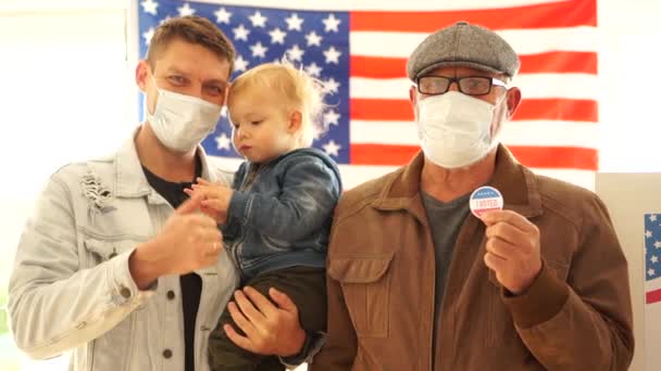 Tres generaciones de la familia americana vinieron a votar en el centro de votación. Padre, hijo y nieto tienen pegatinas para votar. Los hombres usan máscaras protectoras, nosotros las elecciones durante la epidemia de covidio-19 — Vídeo de stock