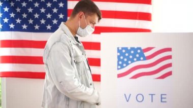 Kot ceketli ve maske takmış genç bir Amerikalı oy kabininde oy kullanıyor. 2020 ABD seçimleri covid-19 coronavirüs salgını sırasında