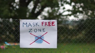 Bölge maske takmaktan muaf. Maskeler, şüpheciler ve onların protestoları. Çitteki poster.