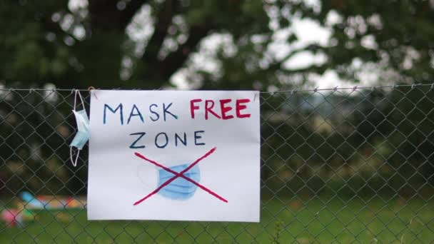 Sulla recinzione è appeso un poster con la maschera di iscrizione zona libera. Un uomo passa e si toglie la maschera. Concetto anti-maschera, covid denier — Video Stock