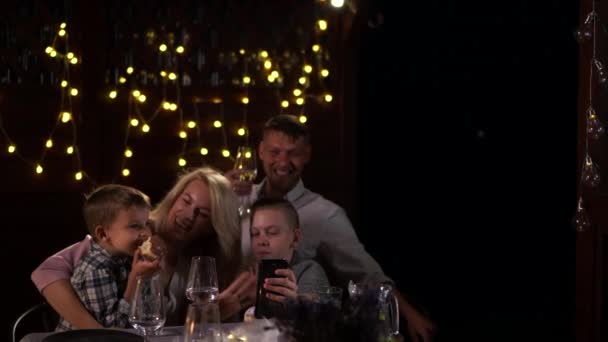 Linda família com dois filhos abraçando enquanto sentado na mesa de Natal no fundo de luzes festivas — Vídeo de Stock