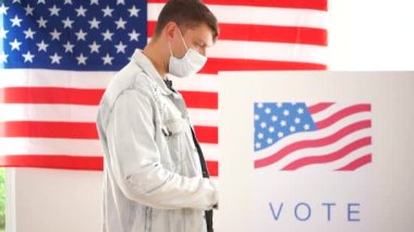 Kot ceketli ve maske takmış bir Amerikalı oy kabininde oy veriyor. 2020 ABD seçimleri covid-19 coronavirüs salgını sırasında