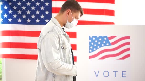 Los ciudadanos estadounidenses votan en un centro de votación durante la cuarentena del coronavirus covid-19. Un hombre y una mujer enmascarados se turnan para acercarse a la cabina de votación. Concepto de elecciones estadounidenses 2020 — Vídeo de stock