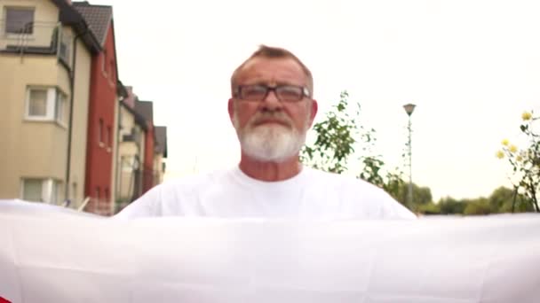 Portret de aproape al unui pensionar cu părul gri, cu ochelari și barbă care deține steagul roșu și alb al Belarusului. Protestul din Belarus, revoluția culorilor — Videoclip de stoc