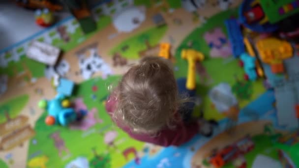 Вид зверху на щасливу дитину, що грає з різнокольоровими іграшками на підлозі на килимі. Щаслива дитина в дитячому садку, дитяче дозвілля — стокове відео