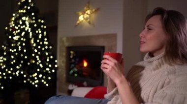 Mutlu Noeller ve mutlu tatiller. Güzel bir genç kız şöminenin yanındaki sandalyede oturuyor ve elinde bir fincan kahve var. Tek kullanımlık fincandan çay içiyor. Yeni yıl arkaplanı