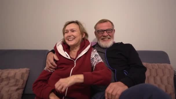 Ein älteres Paar, das auf der Couch sitzt, umarmt sich und lächelt sich an. Glückliches Paar nach Hause Porträt — Stockvideo