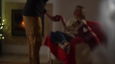 Karı koca, süslü bir arka planda köpekli, sıcak ev kıyafetleri giymiş mutlu bir çift. Yerde oturan bir adam telefonda konuşuyordu. Konforlu bir evde Noel ağacı ve şömine