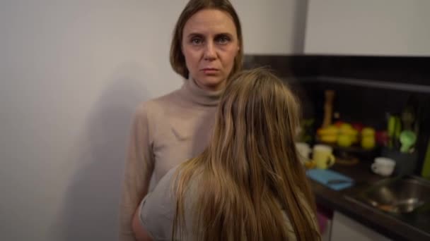 Abused mother and kid. Portrait of a young woman with abrasions on her face holding a teen scared girl. Domestic violence concept. Mother and daughter victims of violence in the kitchen — Stock Video