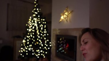 Elinde bir kupa çayla şöminenin ve Noel ağacının arka planında köpek kucaklamalarıyla güzel bir kadın. Mutlu yıllar.