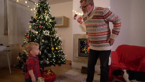 Abuelo y nieto Danza infantil alrededor de la chimenea y el árbol de Navidad. Tradiciones familiares, el anciano y el niño se divierten en Nochebuena — Vídeo de stock