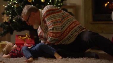 Mutlu büyükbaba ve torun Noel ağacının yanındaki halıya uzanıyorlar. Yaşlı bir adam ve küçük bir çocuk şöminenin yanında oynarken eğleniyorlar, aile gelenekleri.