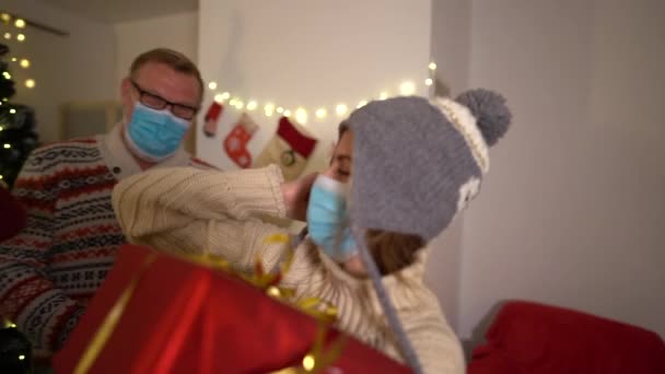 Ευτυχισμένη οικογένεια συναντά τα Χριστούγεννα covid-19 πανδημία. Μητέρα, πατέρας και κόρη φορούν προστατευτικές ιατρικές μάσκες. Κοινωνική απόσταση απομόνωσης καραντίνας. Πρωτοχρονιάτικες διακοπές. Εορταστική διάθεση 2021during κλείδωμα — Αρχείο Βίντεο
