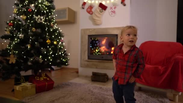 Uma criança bonita está dançando em casa perto da lareira e da árvore de Natal. Celebrando o Natal ou ano novo, infância feliz — Vídeo de Stock