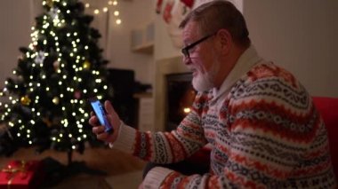 Akıllı telefonlu yaşlı adam yılbaşı ağacının yanında bir video görüşmesi yaptı.