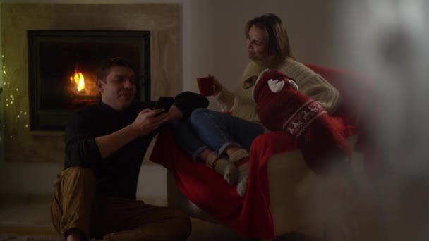 Un hombre y una mujer y su perro están sentados junto a la chimenea. Noche de Navidad. Acogedora víspera de Año Nuevo, familia feliz — Vídeos de Stock