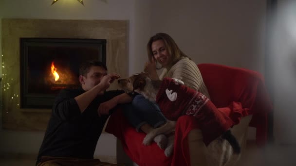 Família feliz, marido e mulher perto da lareira. A mulher ri-se. Celebrando o Natal em casa, veja através de uma janela com padrões gelados. Gelo na janela — Vídeo de Stock