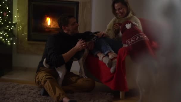 Celebrando la Navidad en casa, vea a través de una ventana con patrones helados. Hielo en la ventana. Familia feliz, marido y mujer cerca de la chimenea — Vídeo de stock