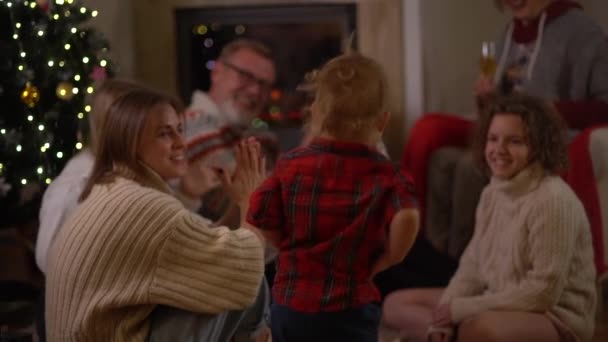 Familia familiar multigeneracional de Navidad reunida junto a la chimenea en Nochebuena. Padres mayores, hija adulta, nietas adolescentes ven bailar al pequeño nieto — Vídeos de Stock