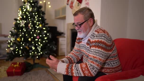 Der alte Mann mit dem Smartphone telefoniert in der Nähe des Weihnachtsbaums