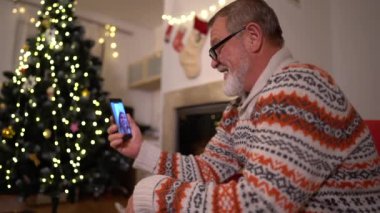 Akıllı telefonlu yaşlı adam yılbaşı ağacının yanında bir video görüşmesi yaptı.