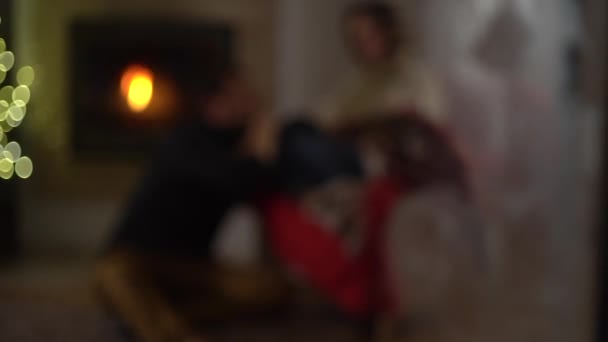 Man en vrouw in een gezellig huis praten met elkaar zittend bij de open haard tegen de achtergrond van een kerstboom. Vorst op het raam, comfort thuis — Stockvideo