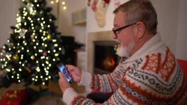 Akıllı telefonlu yaşlı adam yılbaşı ağacının yanında bir video görüşmesi yaptı.