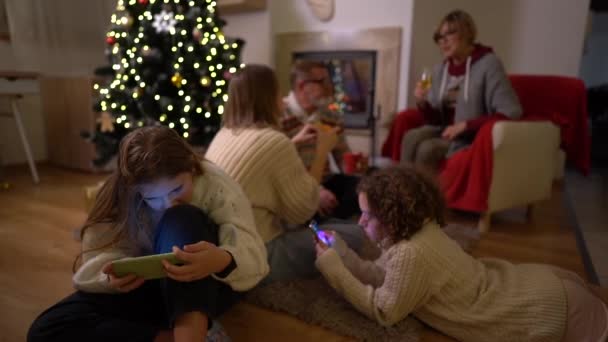 Gençler aile Noel kutlaması sırasında akıllı telefon kullanırlar. Şöminenin yanındaki büyük aile ve Noel ağacı Noel için süslenmiş. — Stok video