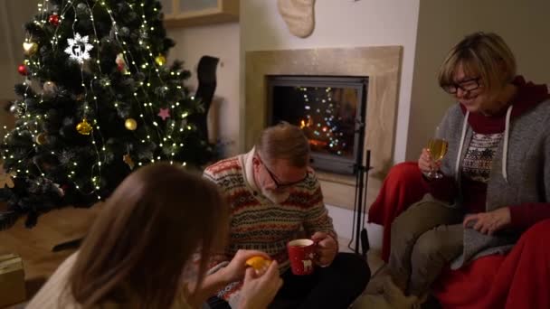 An adult daughter is celebrating Christmas with her elderly parents. A friendly family near the fireplace and the Christmas tree. Family traditions — Stock Video