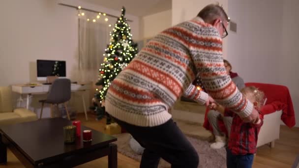 Glad farfar och sonson dansar nära julgranen. En stor familj firar julafton hemma vid öppna spisen. Mysigt hem — Stockvideo