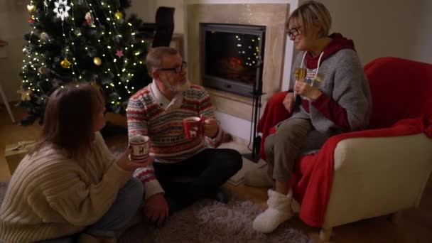 Christmas Eve with family. Elderly parents and their daughter celebrate Christmas together sitting at home by the fireplace against the background of a decorated Christmas tree — Stock Video