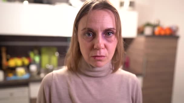 Portræt af en kvinde med et blåt øje og en splittet læbe i køkkenet. Begrebet vold i hjemmet – Stock-video