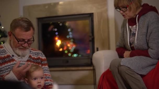 Christmas Eve, happy childhood. Grandparents sit by the fireplace with their little grandson in the living room decorated for Christmas — Video Stock