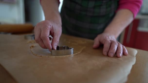 Lebkuchen, selbst gebackene Plätzchen. Nahaufnahme einer älteren Frau, die mit einer Metallform auf fettdichtem Papier Shortbread-Kekse backt — Stockvideo