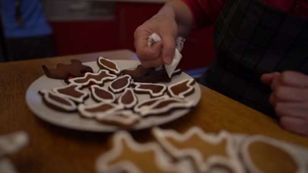 Κοντινό πλάνο ενός χεριού γιαγιάδων που διακοσμεί χριστουγεννιάτικα μπισκότα για τα εγγόνια της με γλάσο ζάχαρης. Οικογενειακές παραδόσεις, σπιτικά ψημένα φαγητά — Αρχείο Βίντεο